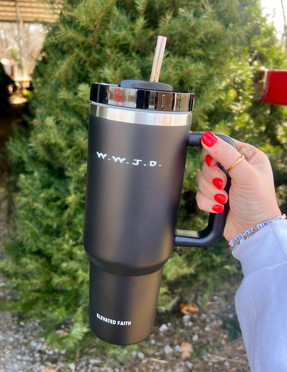 Black insulated tumbler with lid and straw, held by a hand with red nails; WWJD logo.