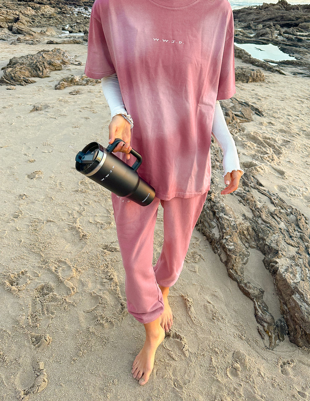 Black insulated tumbler held by a person in a pink outfit; straw through the lid.