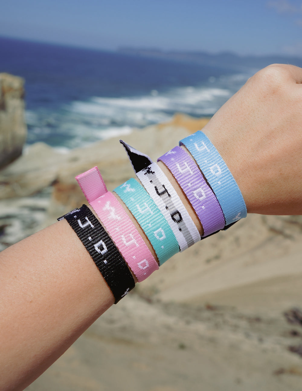 Colorful woven WWJD-style friendship bracelets on an arm near the beach