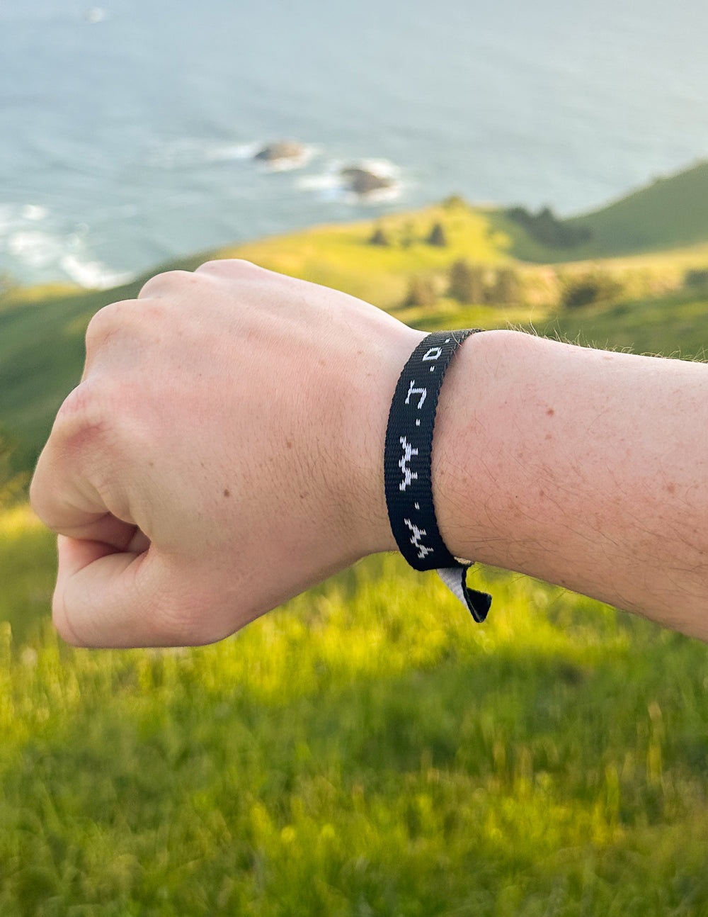 WWJD bracelet on wrist, dark band with light repeating symbol pattern