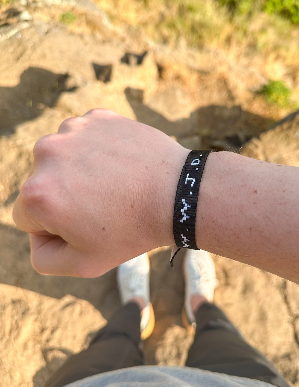 Black fabric WWJD bracelet with white text symbols on wrist