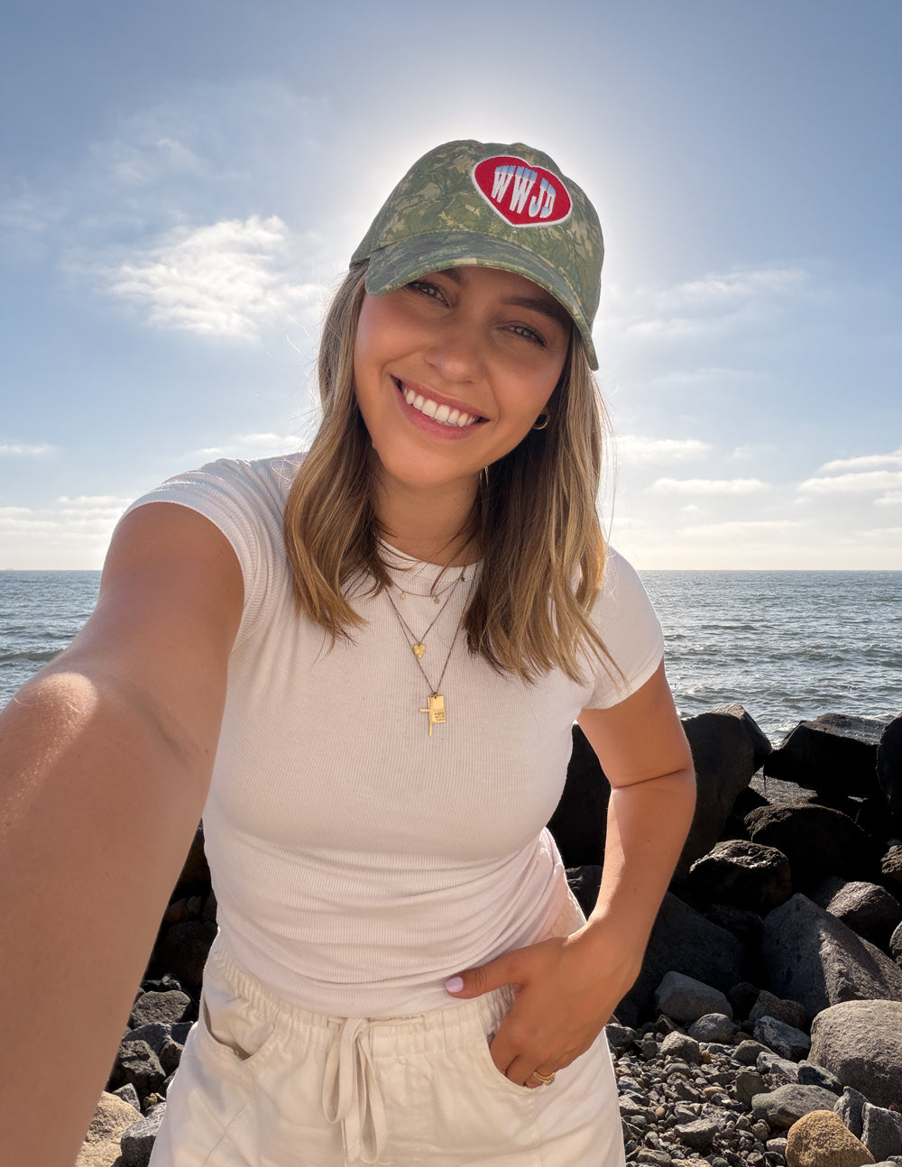 WWJD camo baseball cap with red heart logo patch, worn in outdoor portrait