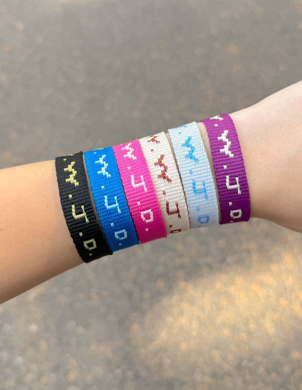 Wrist wearing set of woven cyber charm bracelets in blue, pink, black, and white.