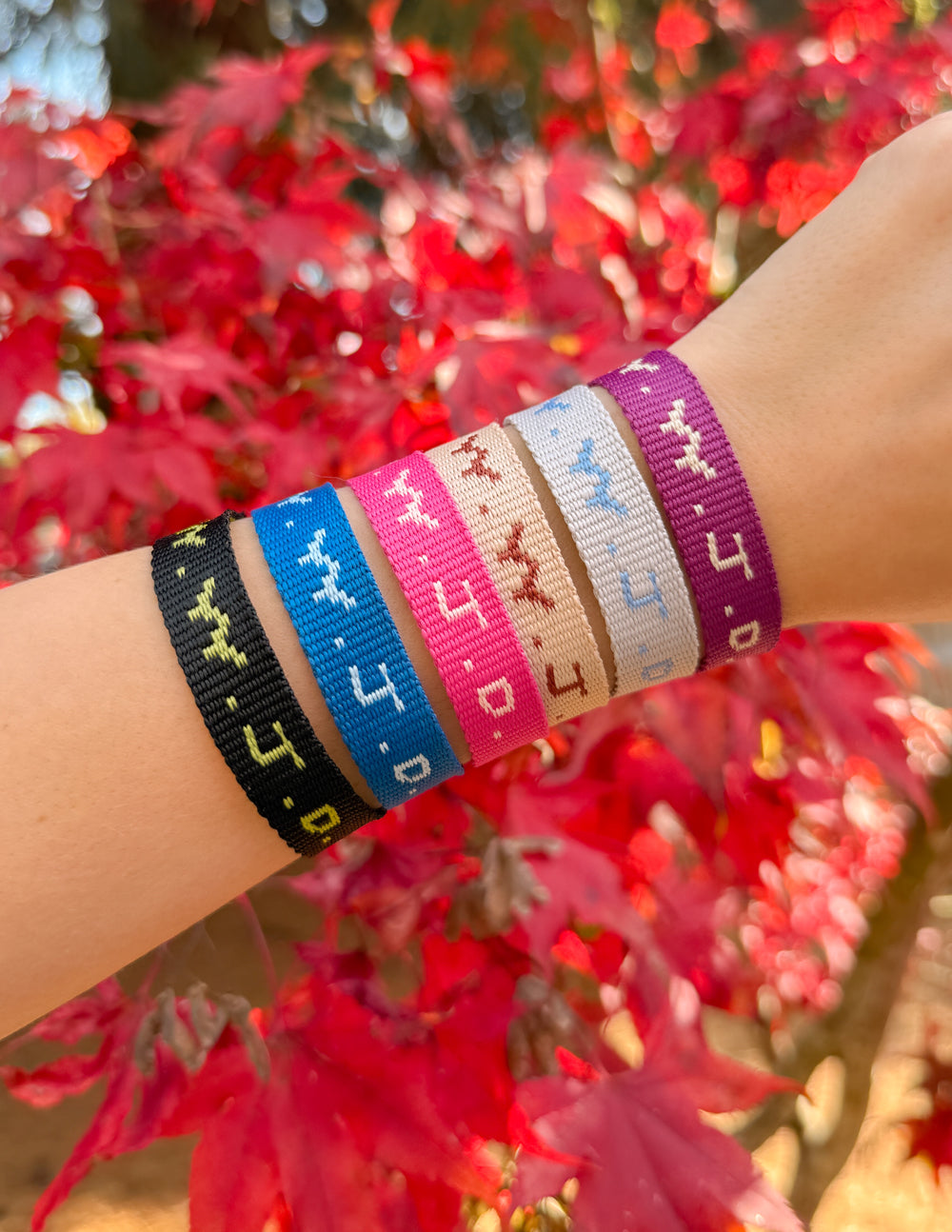 Arm wearing set of woven cyber charm bracelets in blue, purple, beige, black, and white.