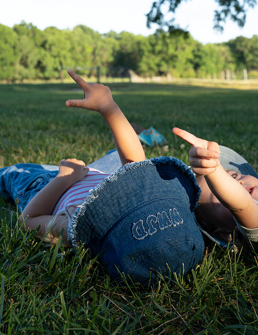 Denim bucket hat lying in grass with embroidered WWJD logo and frayed brim, blue