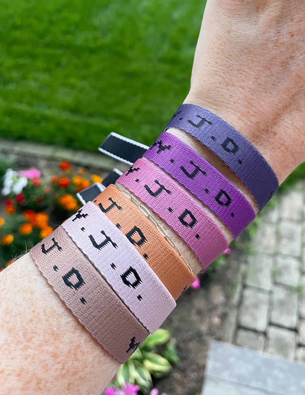 Wrist wearing three WWJD woven bracelets in purple, tan, and lavender with clasp