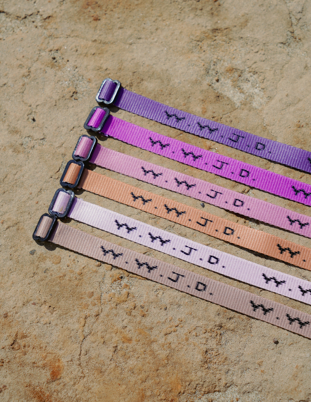 Five WWJD woven adjustable bracelets laid flat in purple, pink, peach, and white tones