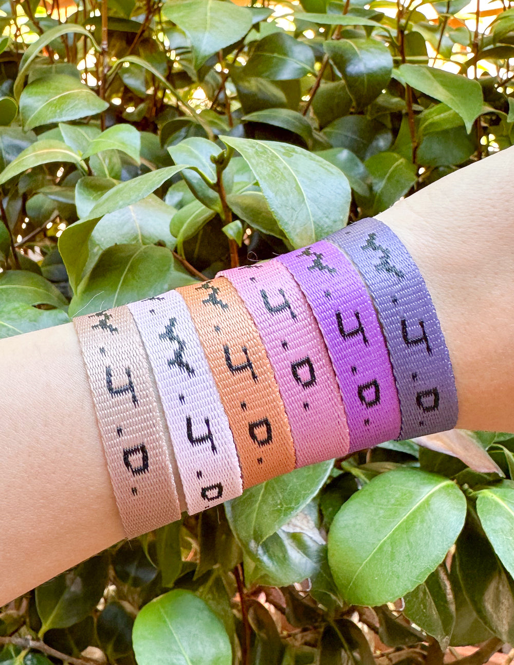 Wrist wearing four WWJD woven bracelets in purple, peach, gray, and white with clasp
