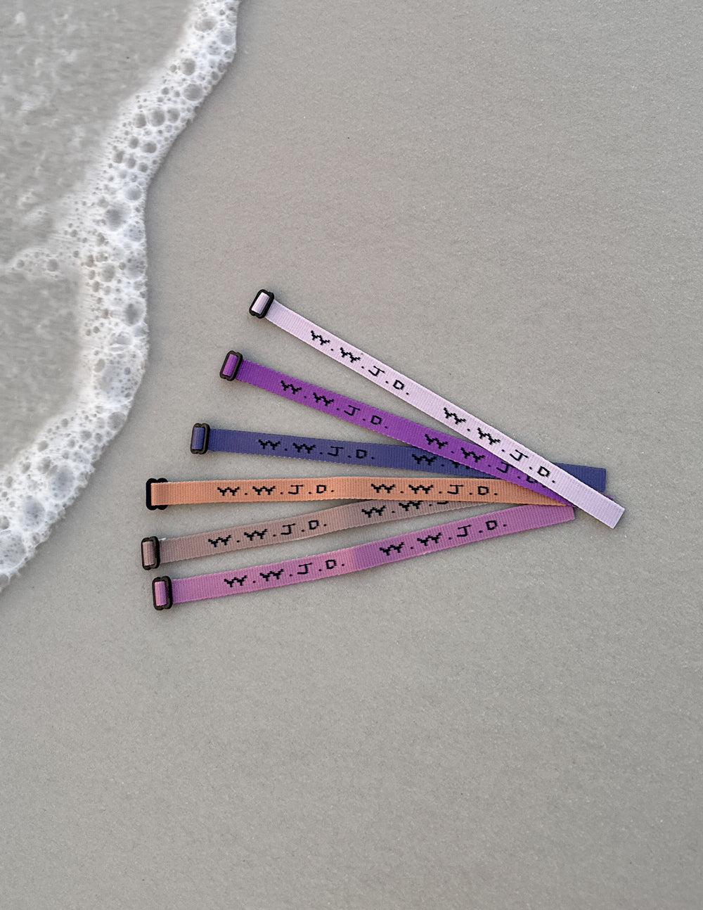 Four WWJD woven adjustable bracelets with metal clasps in purple, pink, tan, and navy
