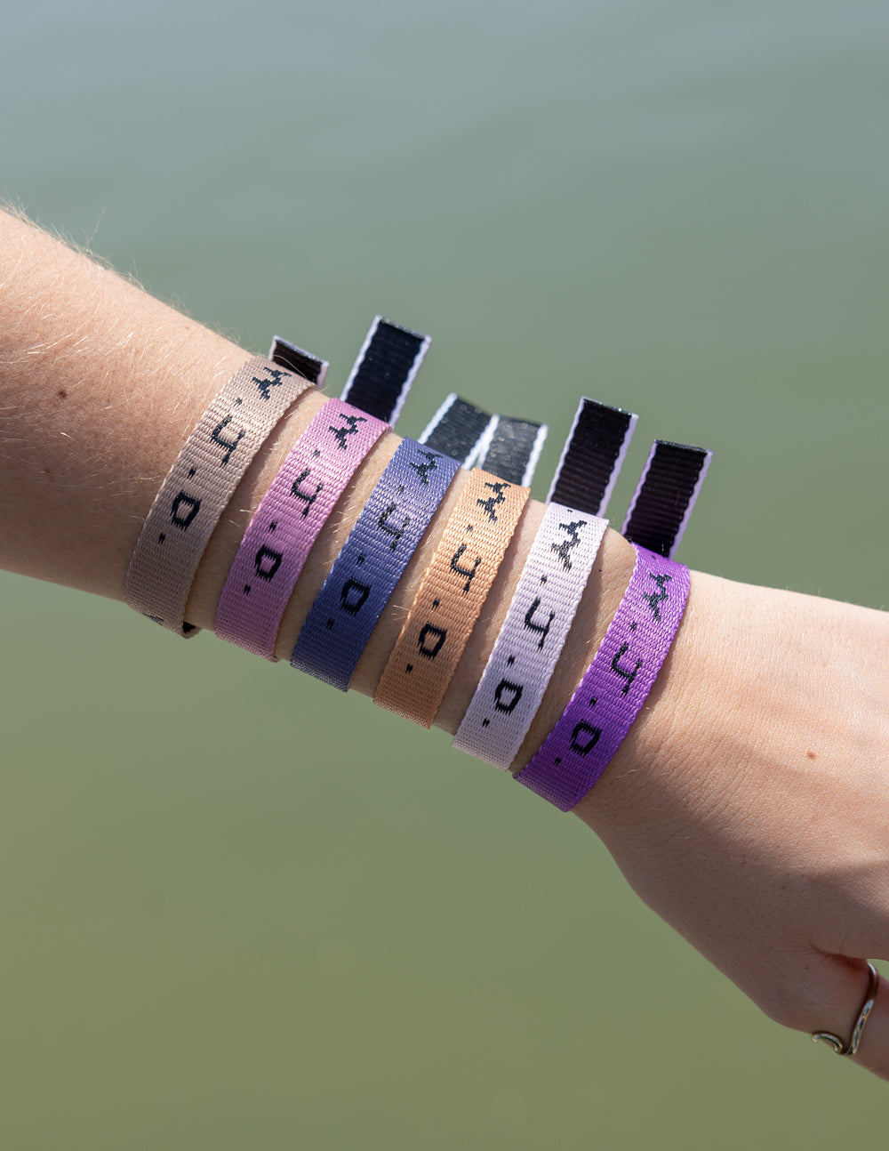 Wrist with five WWJD woven bracelets in taupe, purple, tan, navy, and white tones