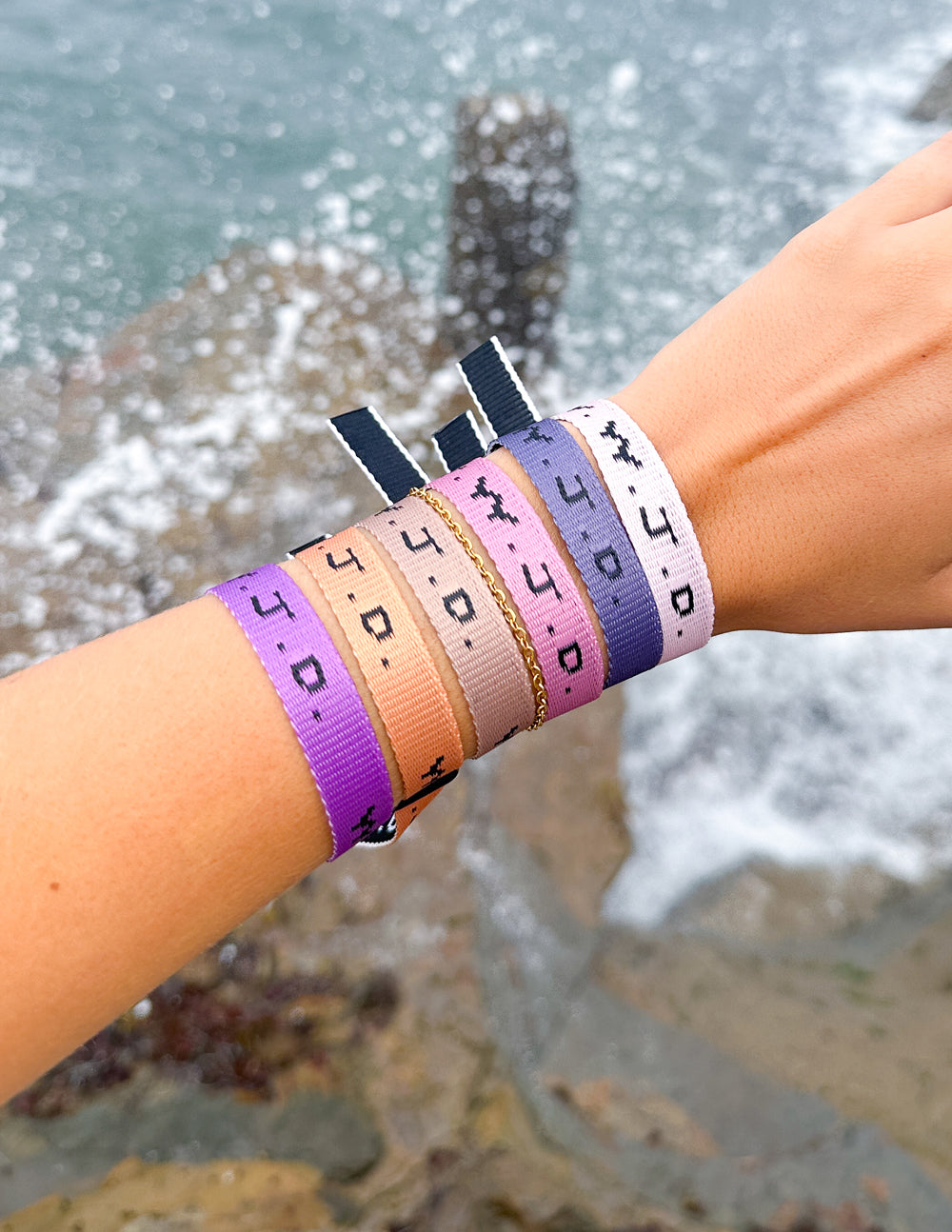 Wrist wearing WWJD woven bracelets in purple and orange with light gray metal clasp
