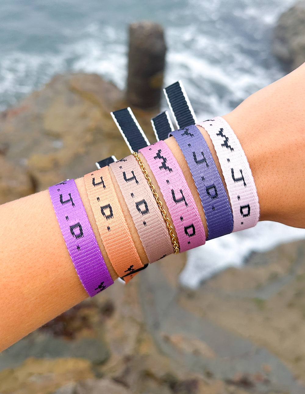 Wrist wearing five WWJD woven bracelets in purple, orange, white, and gray with clasp