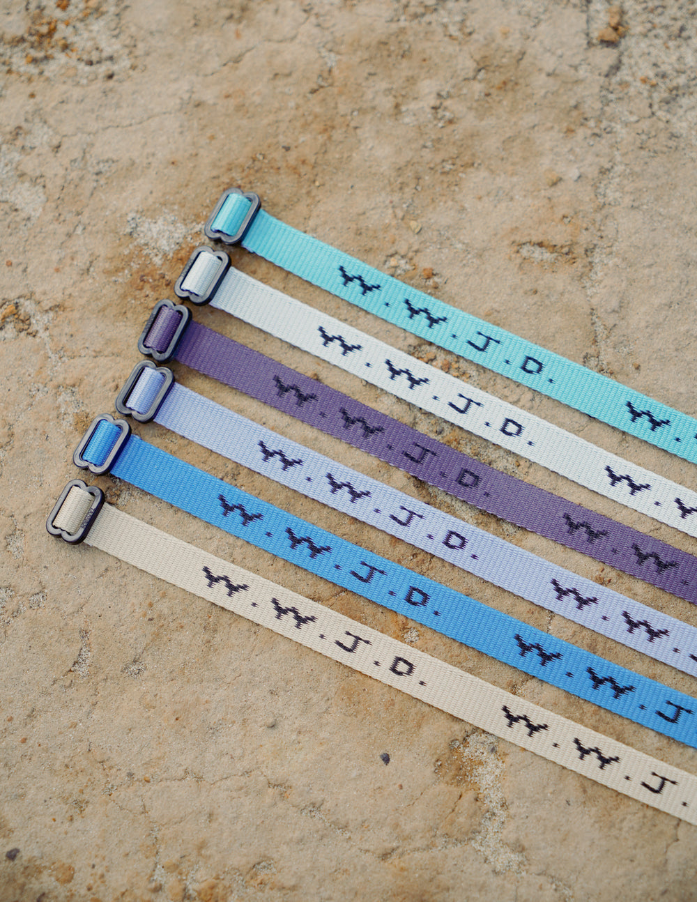 Fabric surf bracelets with WWJD print and adjustable buckles, arranged on stone
