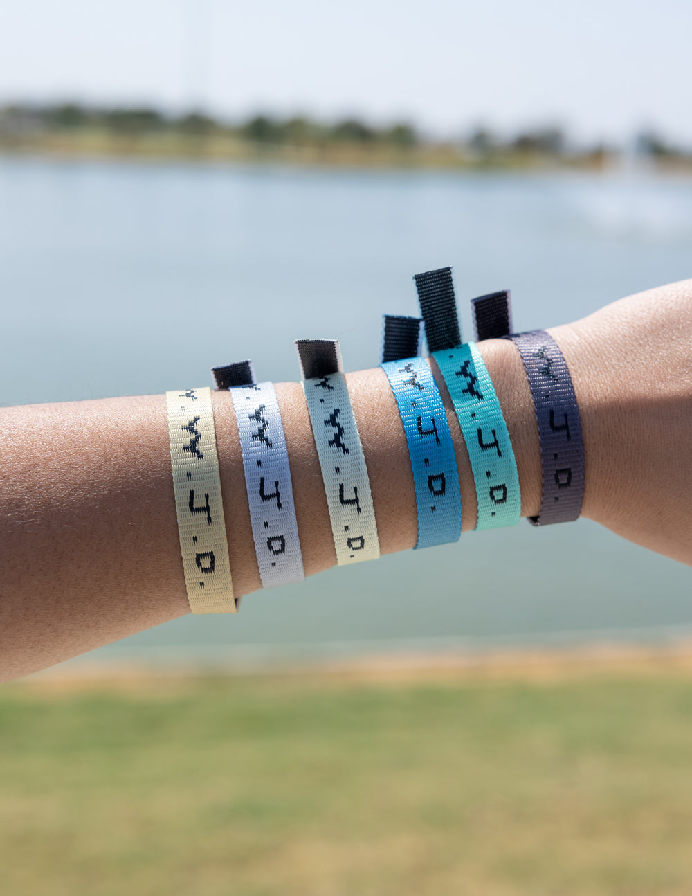 Five fabric surf bracelets with WWJD print on forearm, outdoors by water