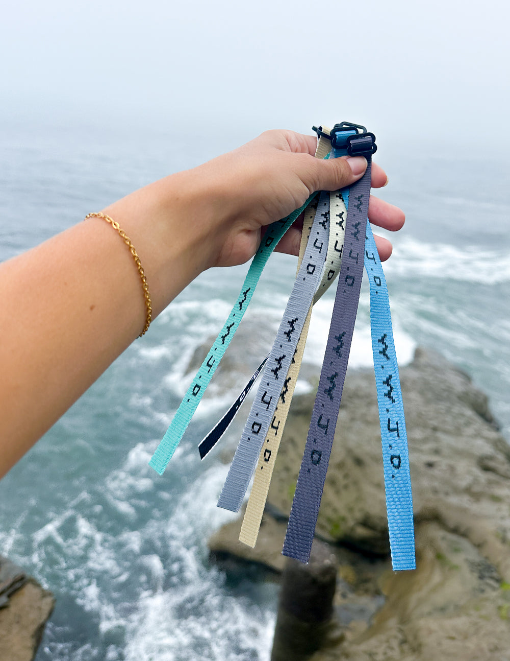 Hand holding multiple fabric surf bracelets with WWJD print and plastic clasps