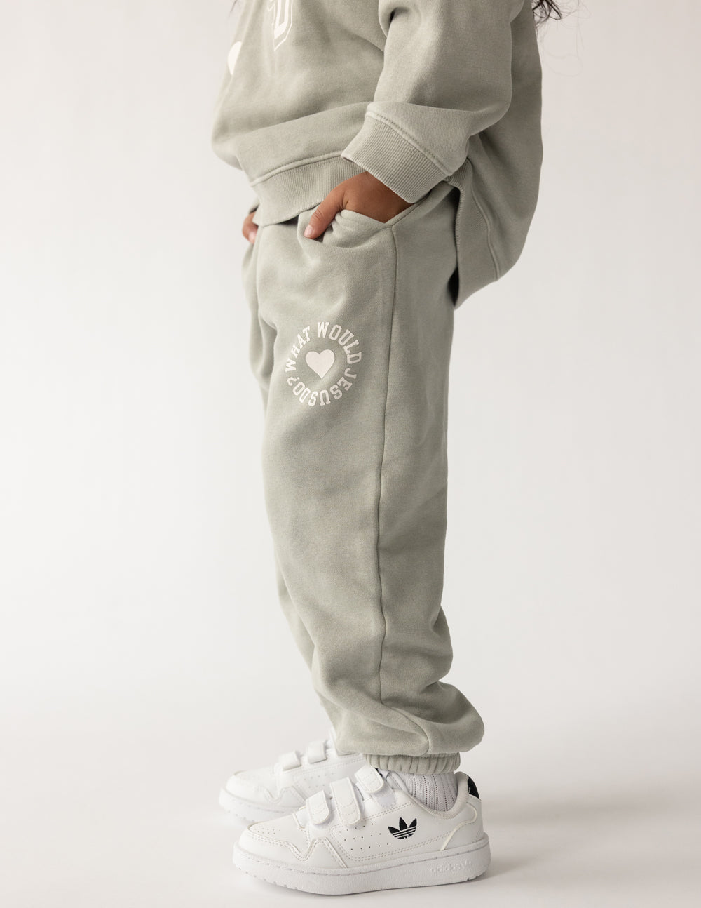 Light gray kids sweatpants with heart logo and elastic waistband, paired with sneakers