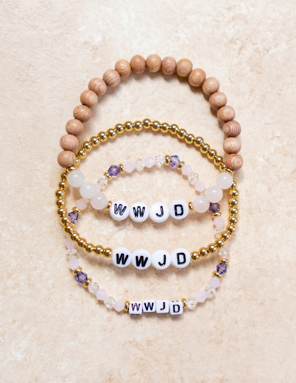 Stacked WWJD letter bracelets with wood beads, gold chain beads, and purple crystal charms