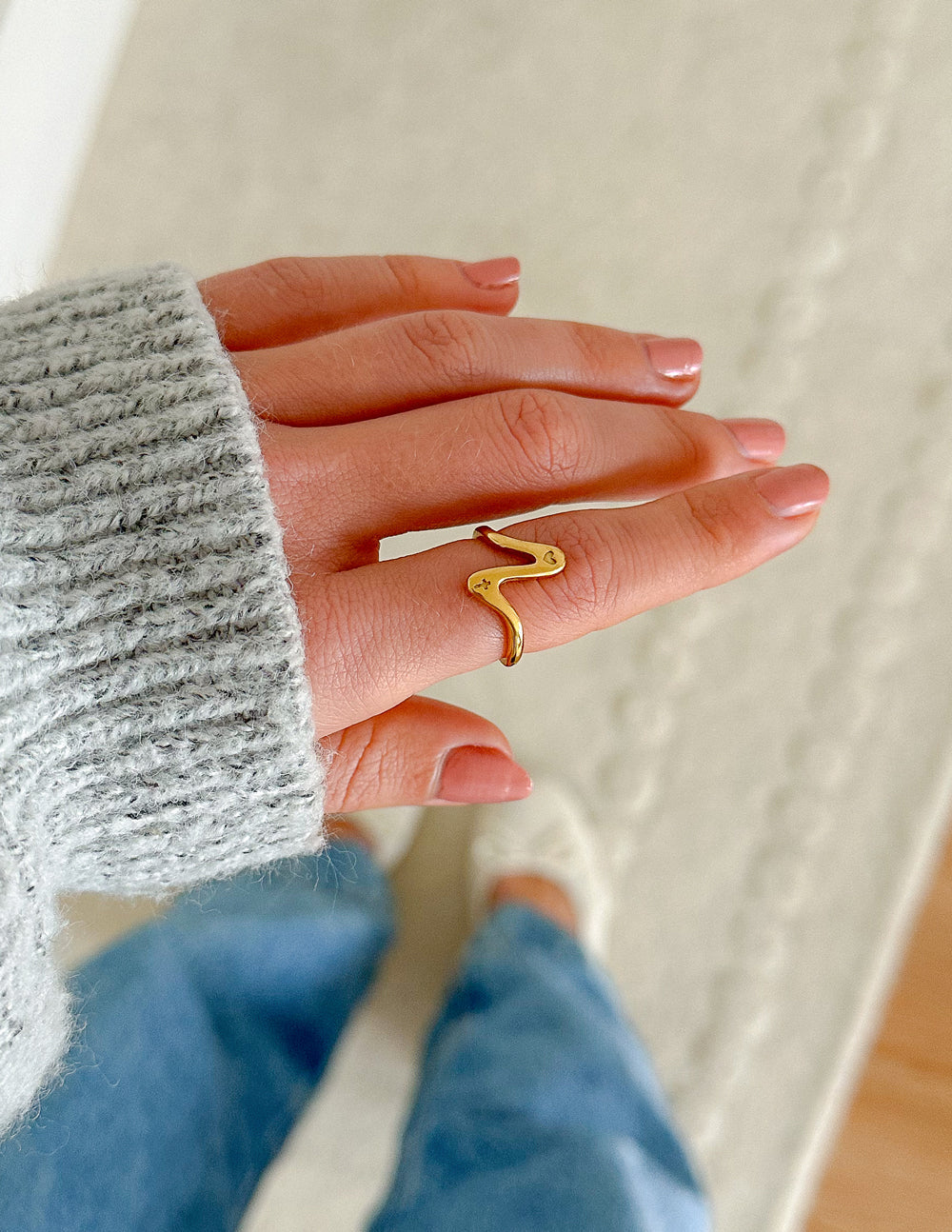 Gold wavy heart ring worn on finger, open cutout heart design