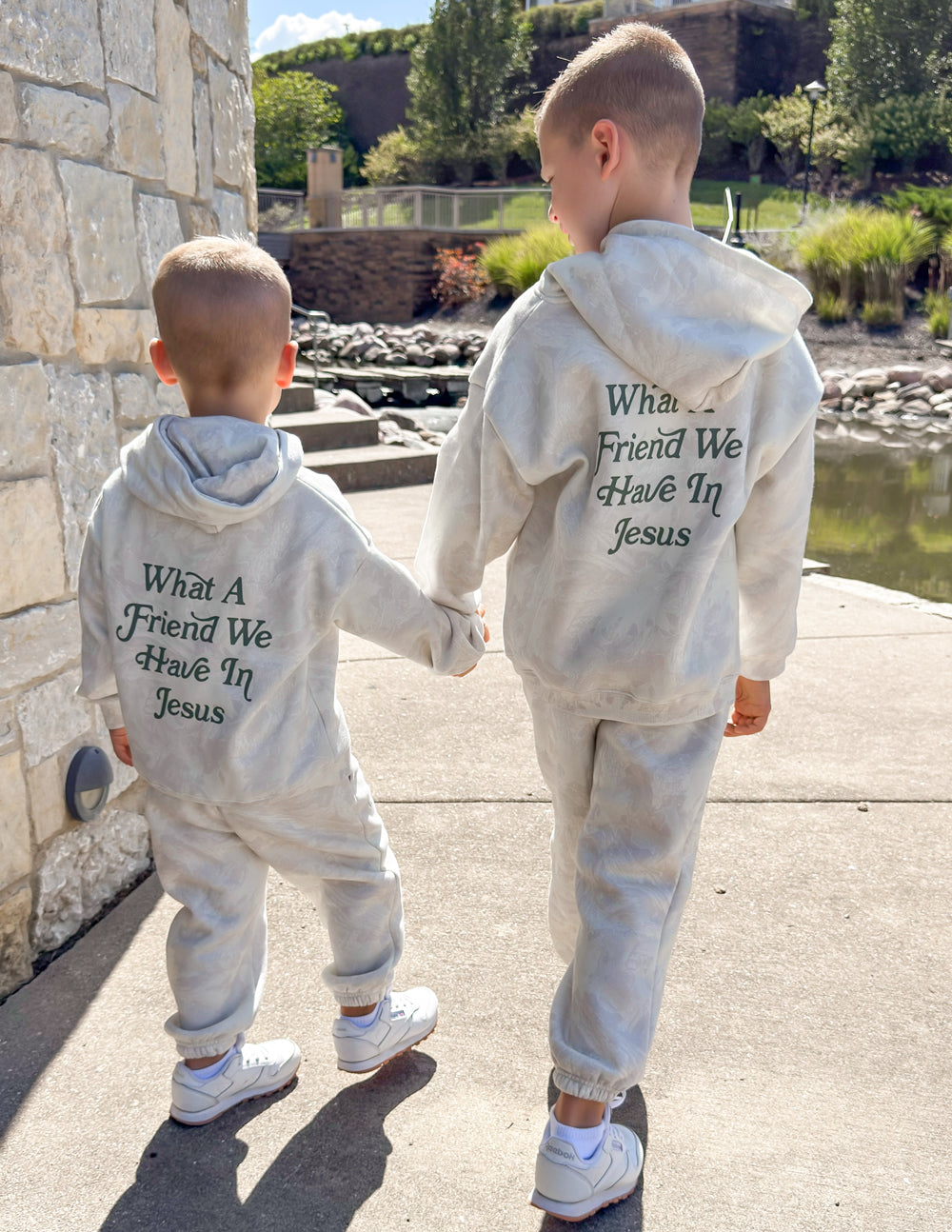 Kids matching pullover hoodies in light gray, both with back graphic text “What A Friend We Have In Jesus”.