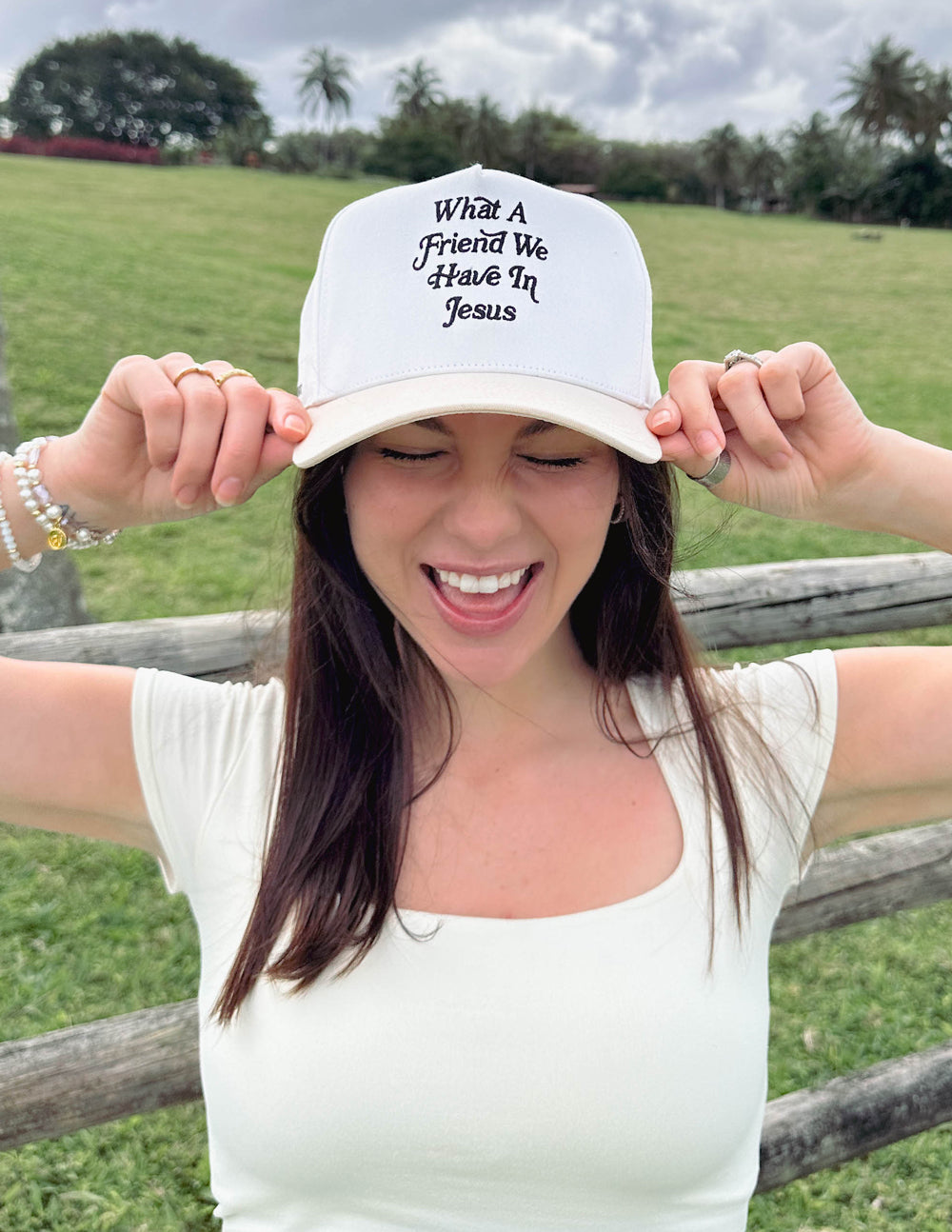 White trucker hat being adjusted, featuring “What a Friend We Have In Jesus” embroidery