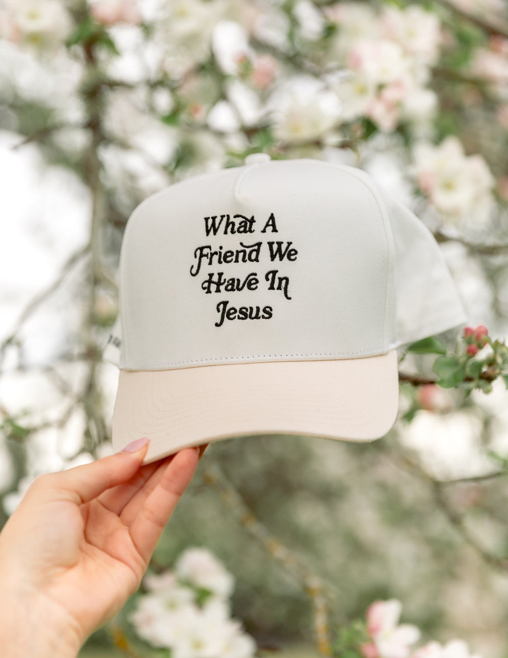 Front view of white trucker hat with “What a Friend We Have In Jesus” embroidery