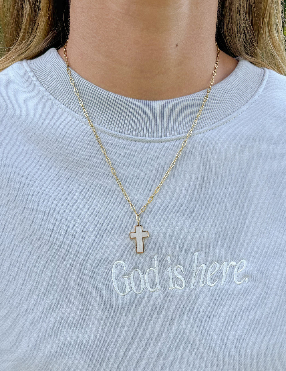 Gold cross necklace with white enamel cross pendant, shown on neckline