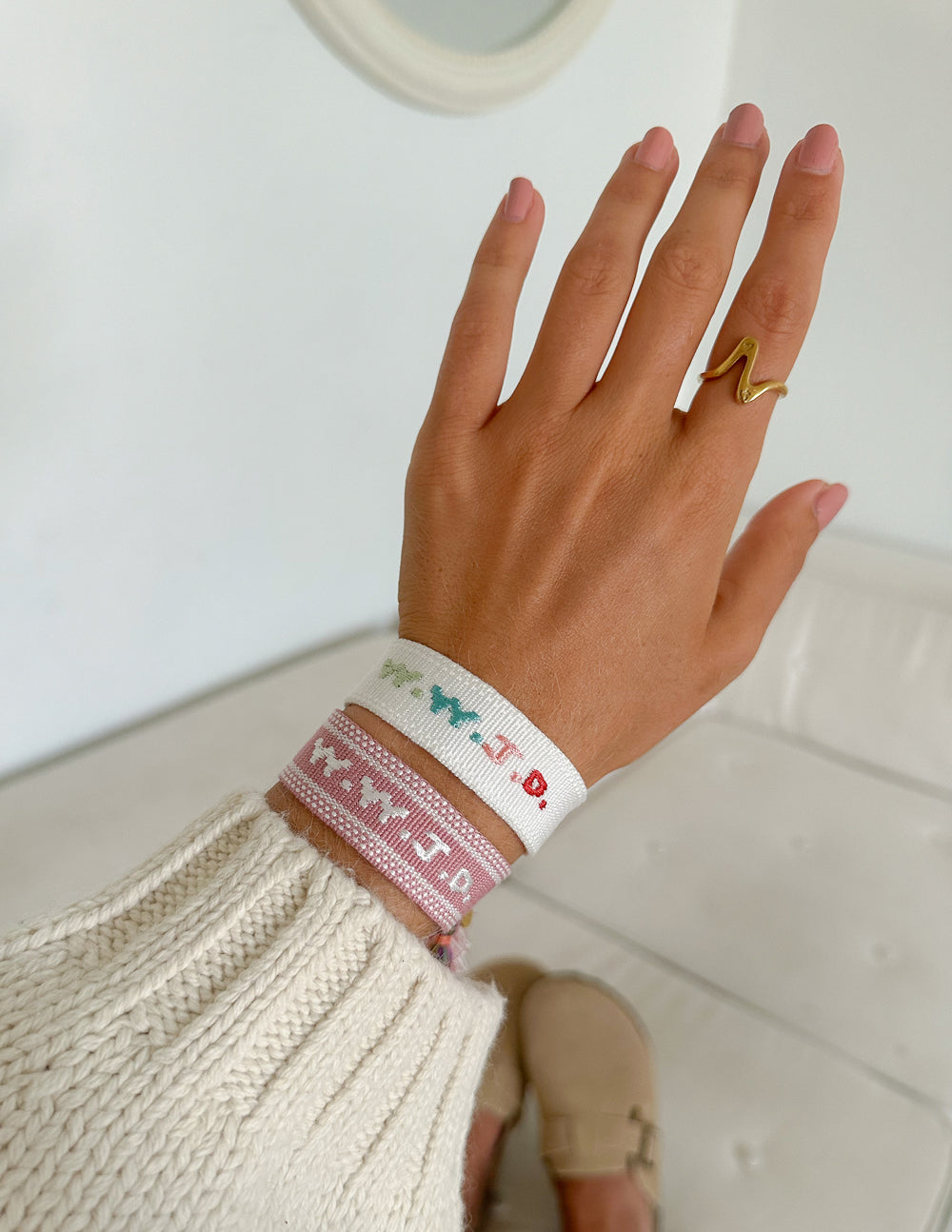 Pink and white woven bracelet with turquoise and red embroidered letters on wrist