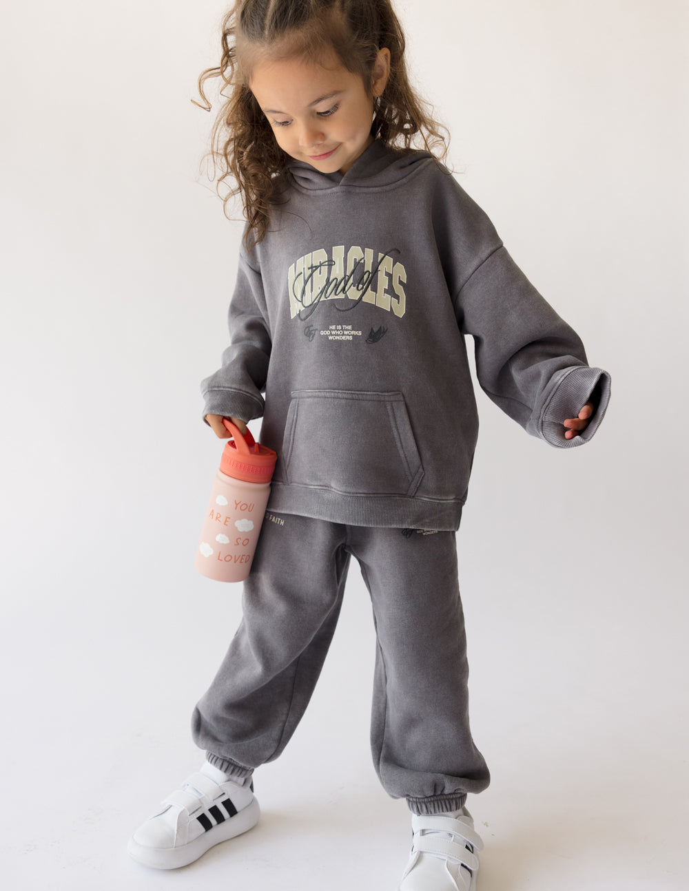 Kids water bottle in pink with orange lid, held by a child in a hoodie.