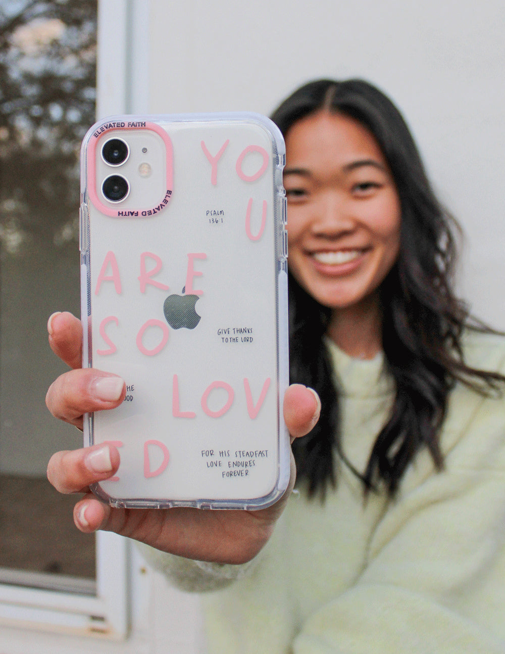 Clear phone case with pink lettering and four camera cutouts, shown beside a face
