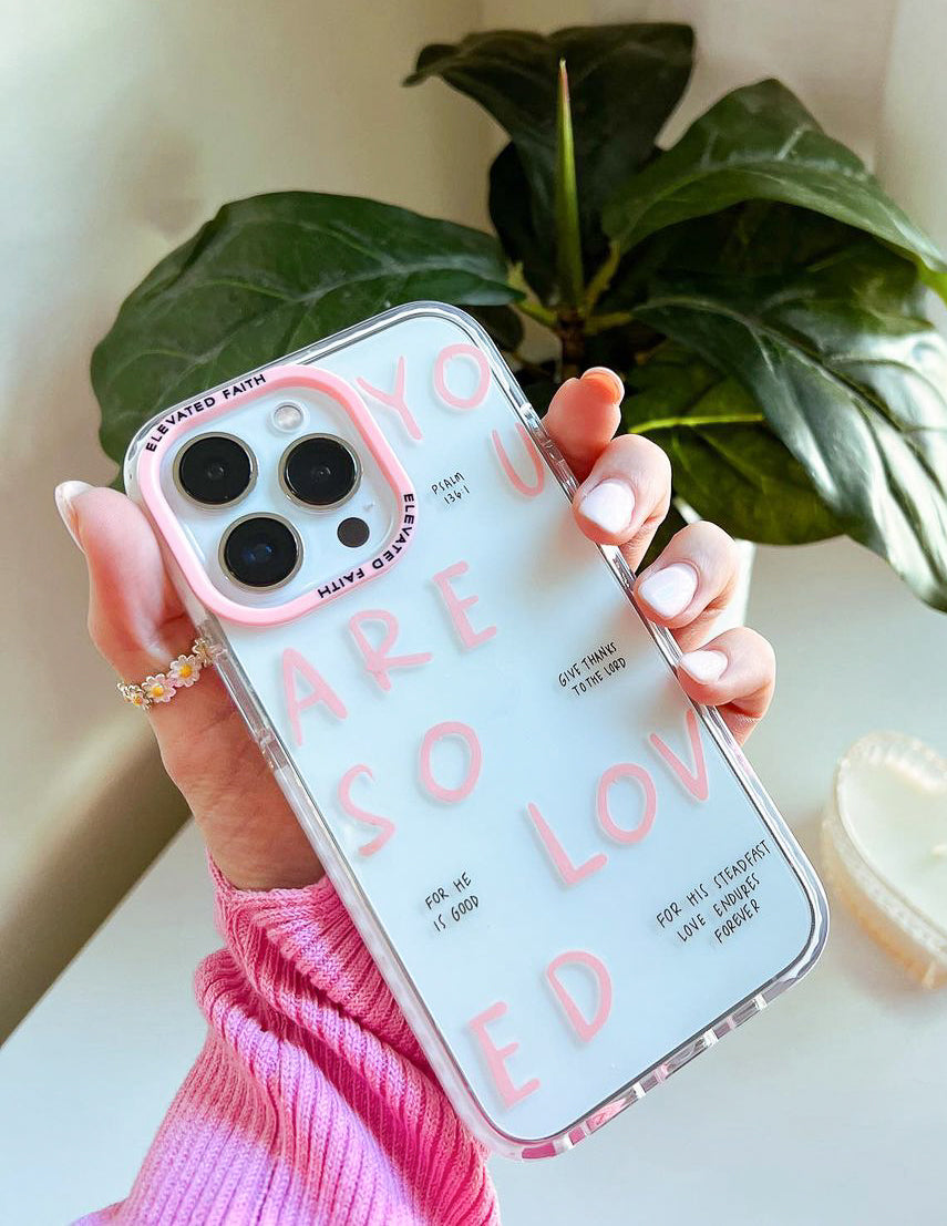 Light pink phone case with clear sides and multi-color heart text; cutouts for cameras.