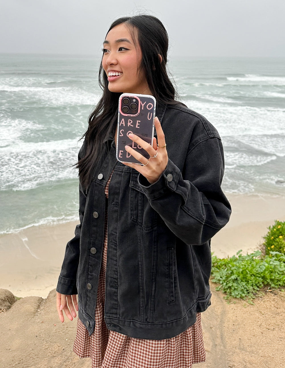 Phone case with pink lettering and four camera cutouts on a person’s phone