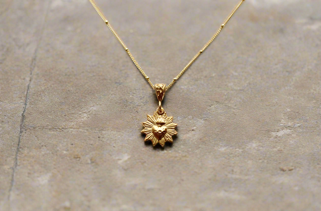 Scalloped necklace with gold sunburst charm pendant on thin chain, smooth polished look