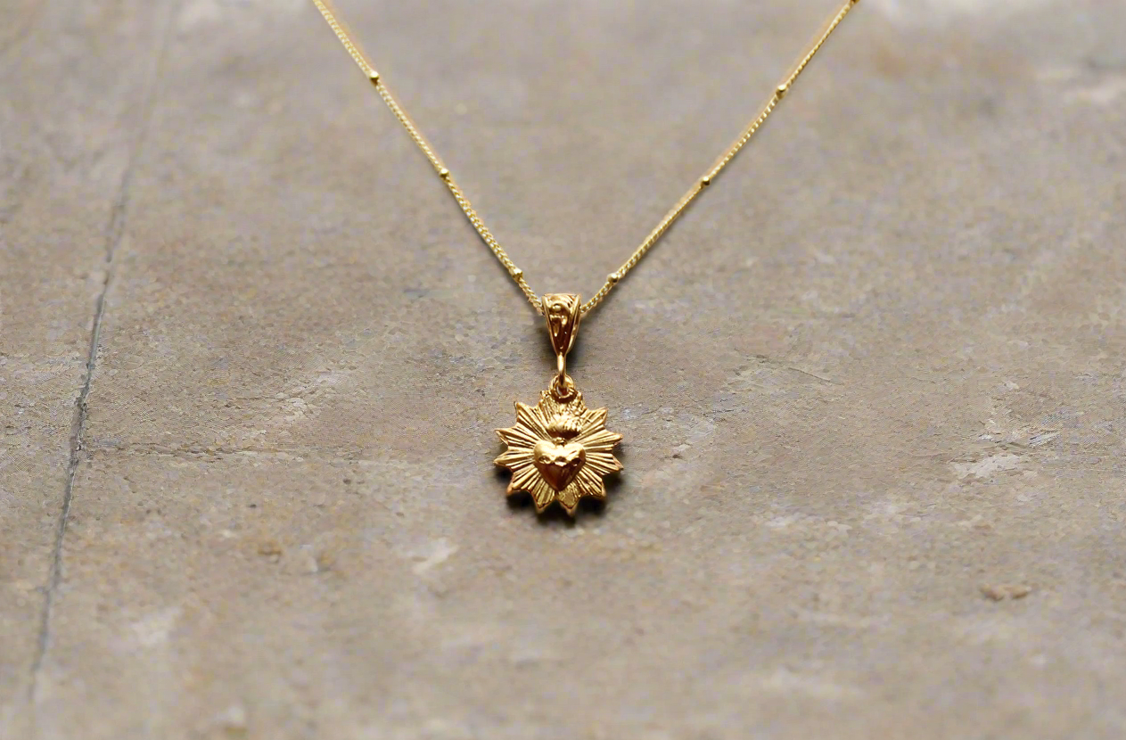 Scalloped necklace with gold sunburst charm pendant on thin chain, smooth polished look