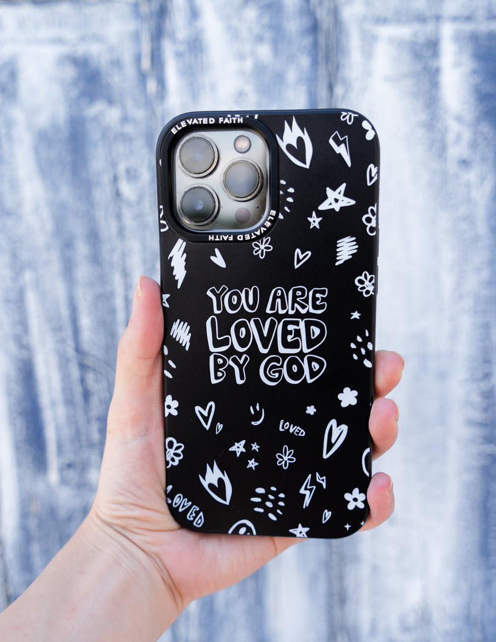 Black phone case held in hand with 'You are loved by God' lettering and white icons