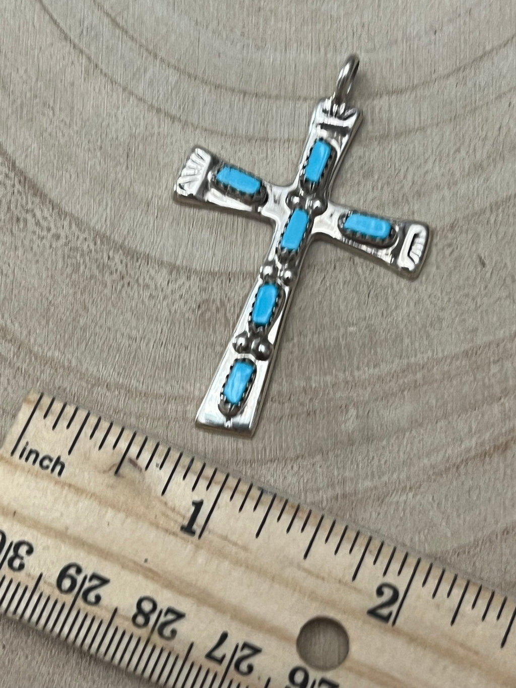 Turquoise cross pendant with silver-tone frame and blue stones, shown with ruler.