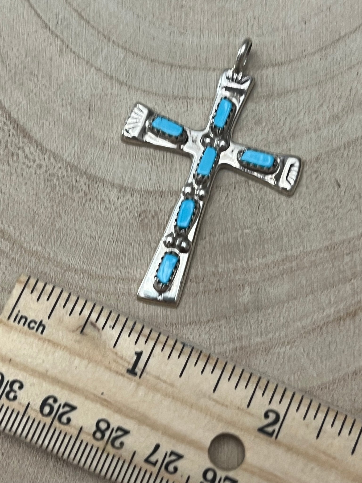 Turquoise cross pendant with silver-tone frame and blue stones, shown with ruler.