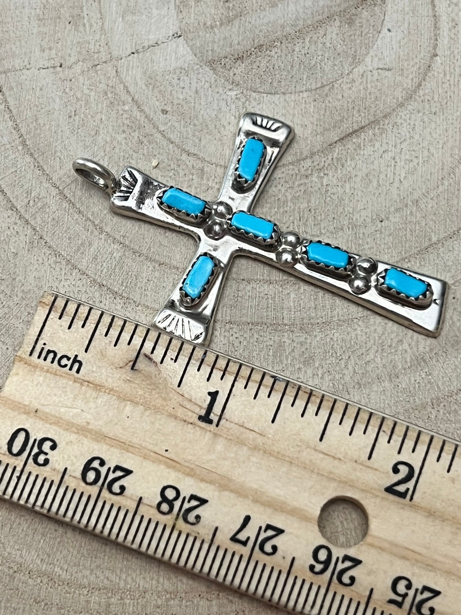 Turquoise cross pendant with silver-tone settings and blue stones, shown by ruler.