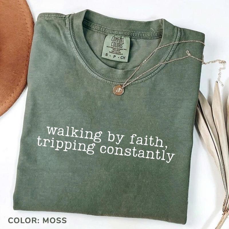 Women’s crewneck graphic tee, moss green with “walking by faith, tripping constantly”
