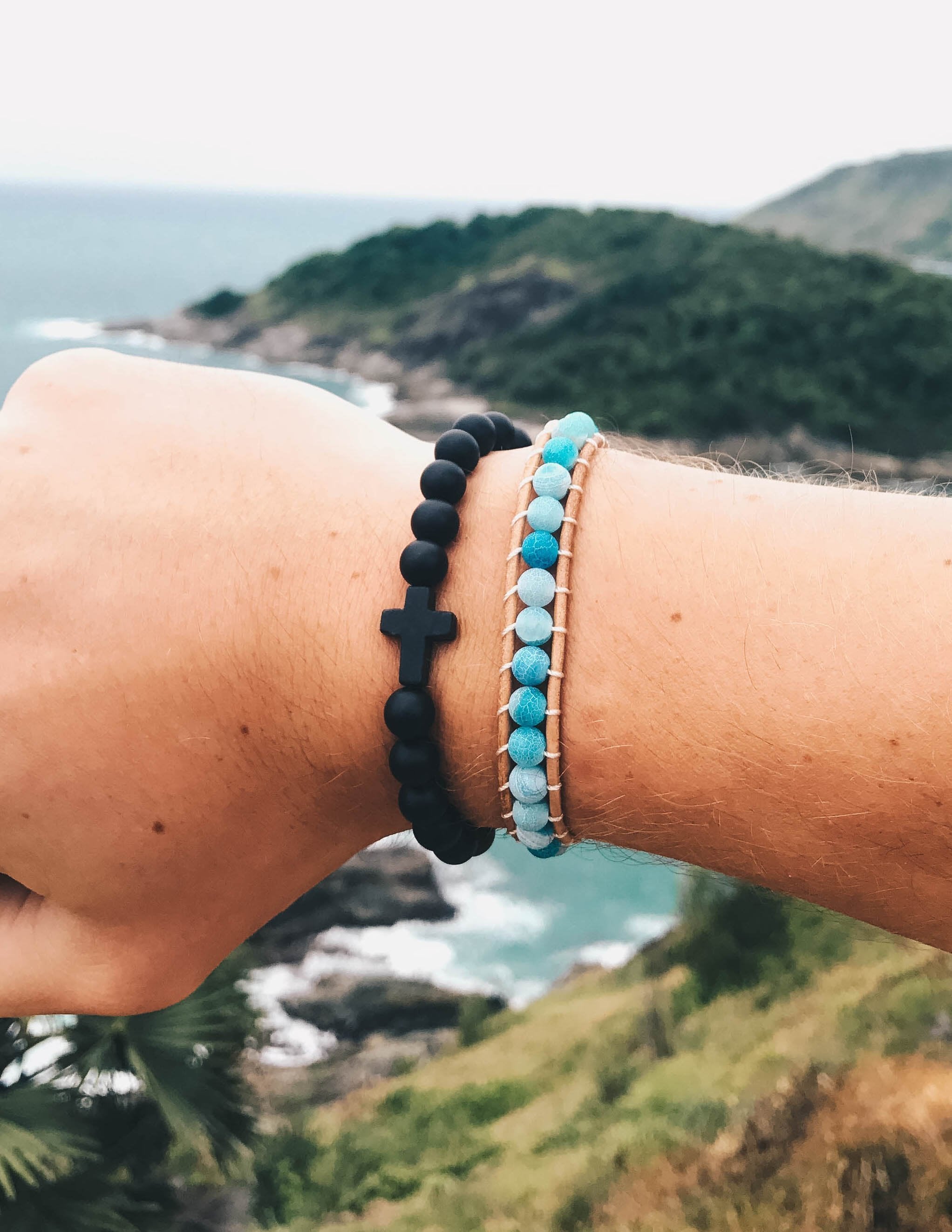 Black beaded cross bracelet on wrist with cross charm, plus turquoise beaded bracelet