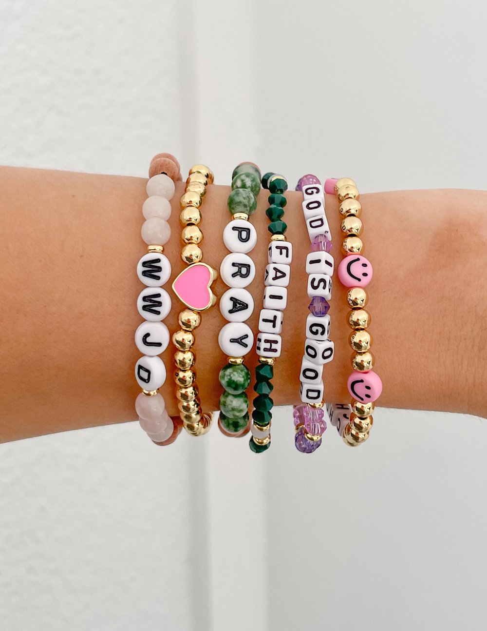 Stacked beaded bracelets with letter beads, gold beads, and pink heart charms