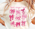 Cream T-shirt with pink script 'God says I am' and ribbon bow graphic