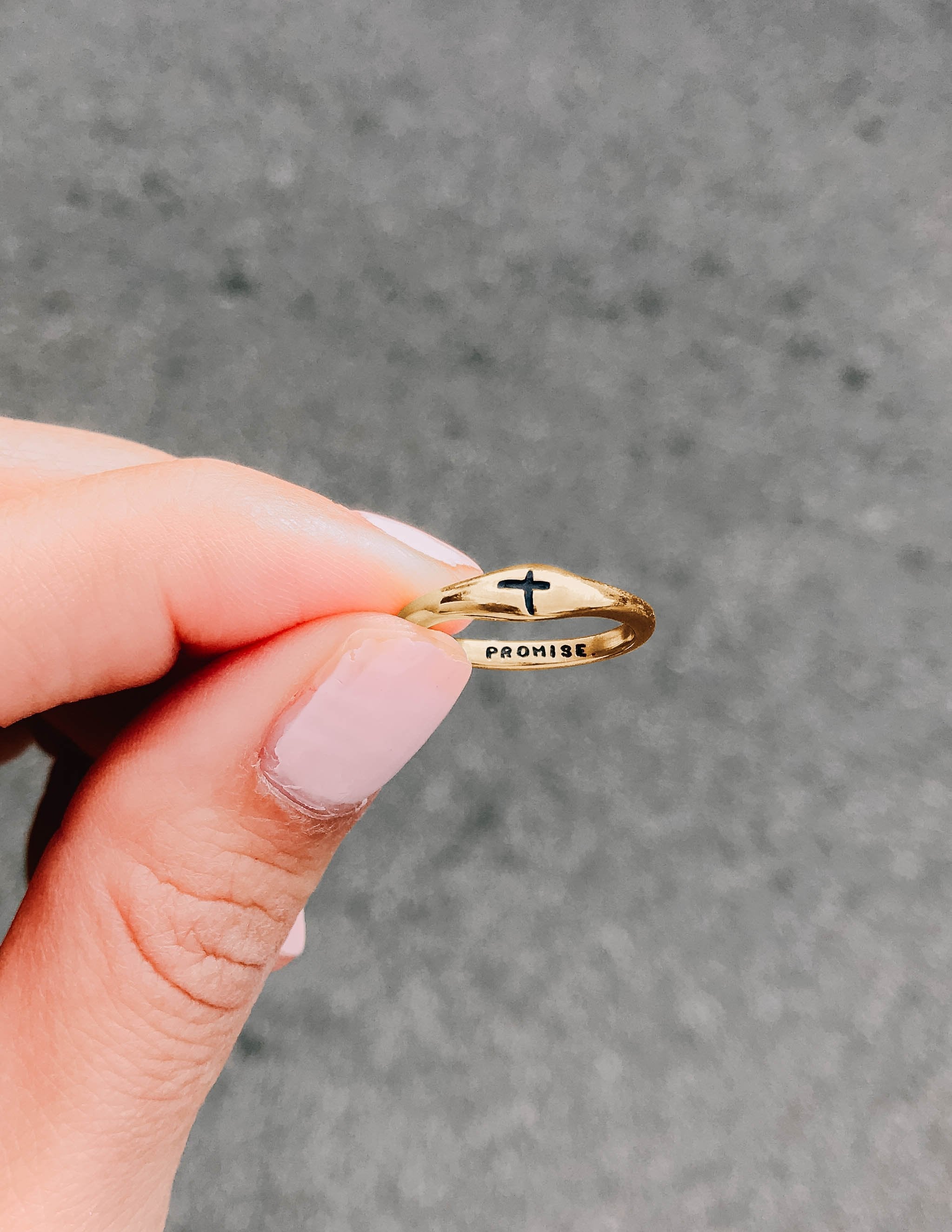Gold ring held in fingers, with cross emblem and 'PROMISE' marking