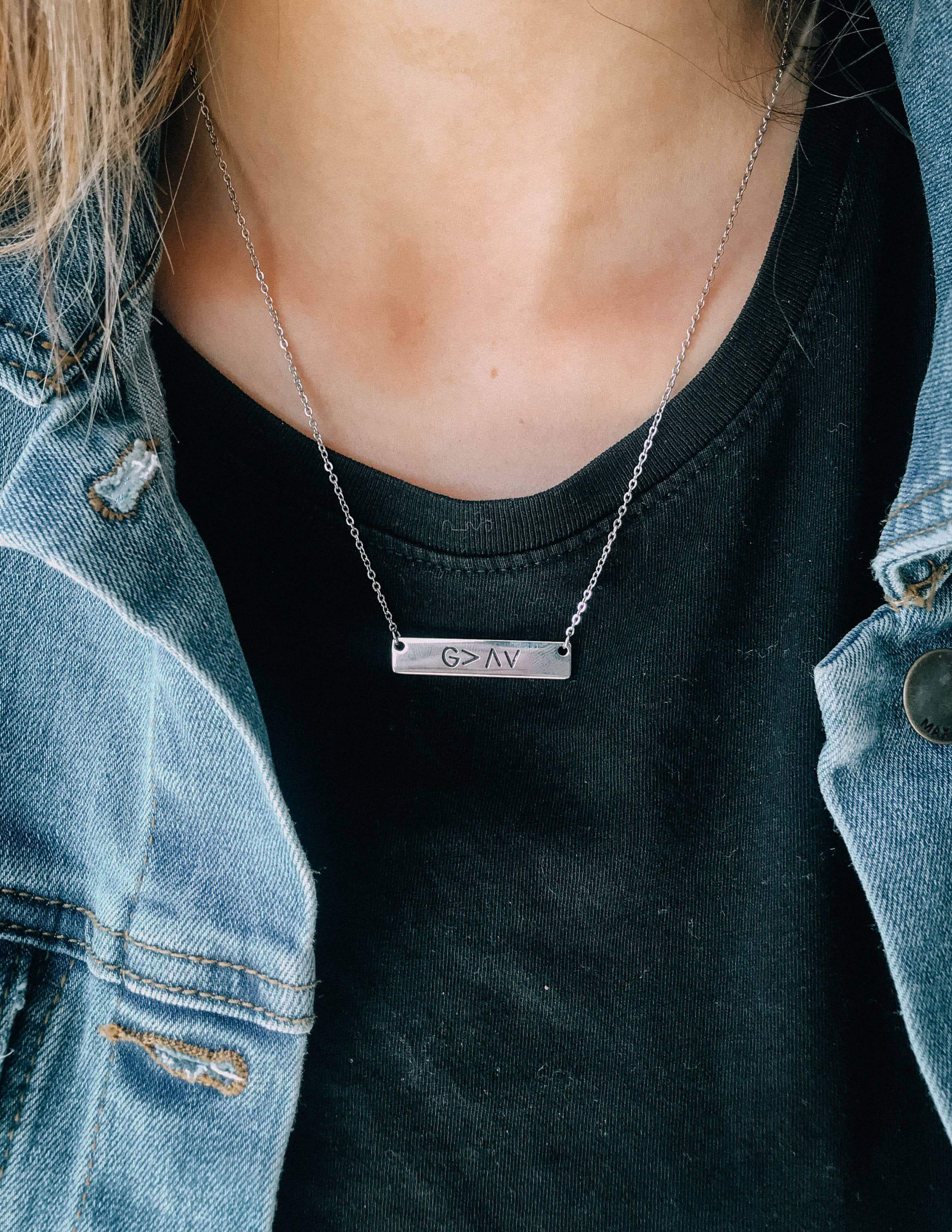 Silver chain pendant necklace with rectangular G>AV bar on black top and denim