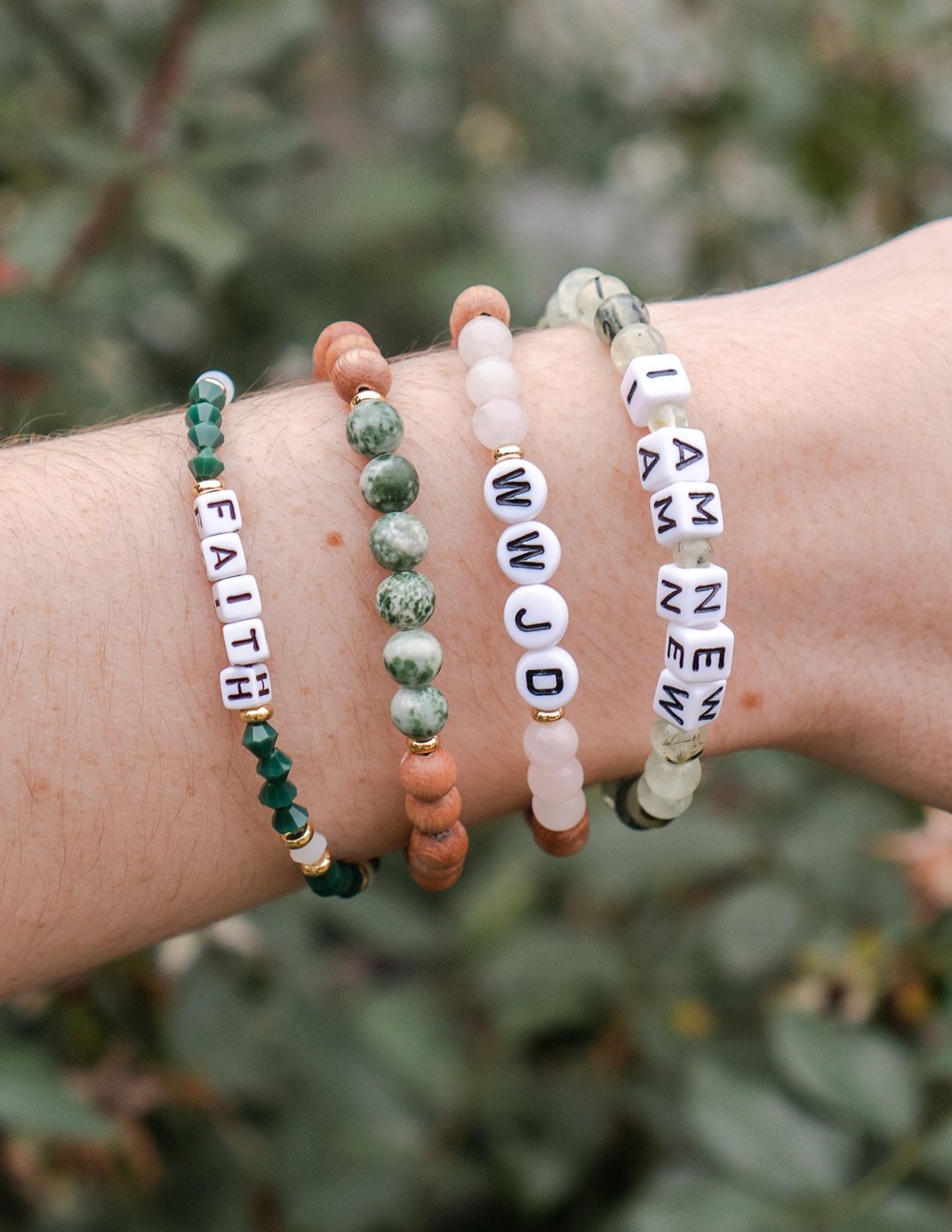 Letter beaded bracelets on wrist with green and white round beads and word charms