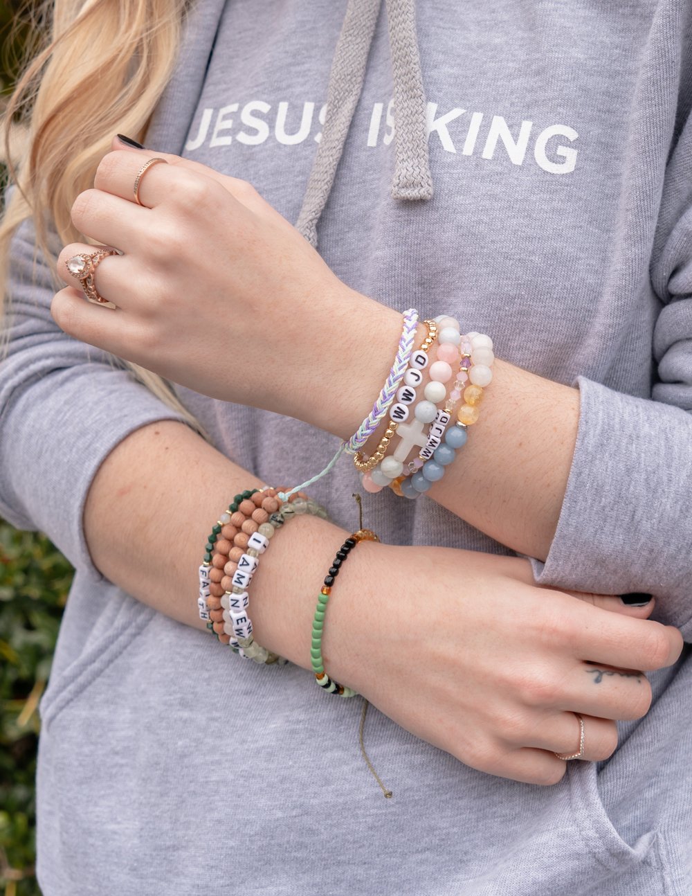 Stack of letter beaded bracelets with white, green, and gold-toned beads on wrist