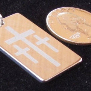 Dog tag pendant with engraved cross design beside a coin for size