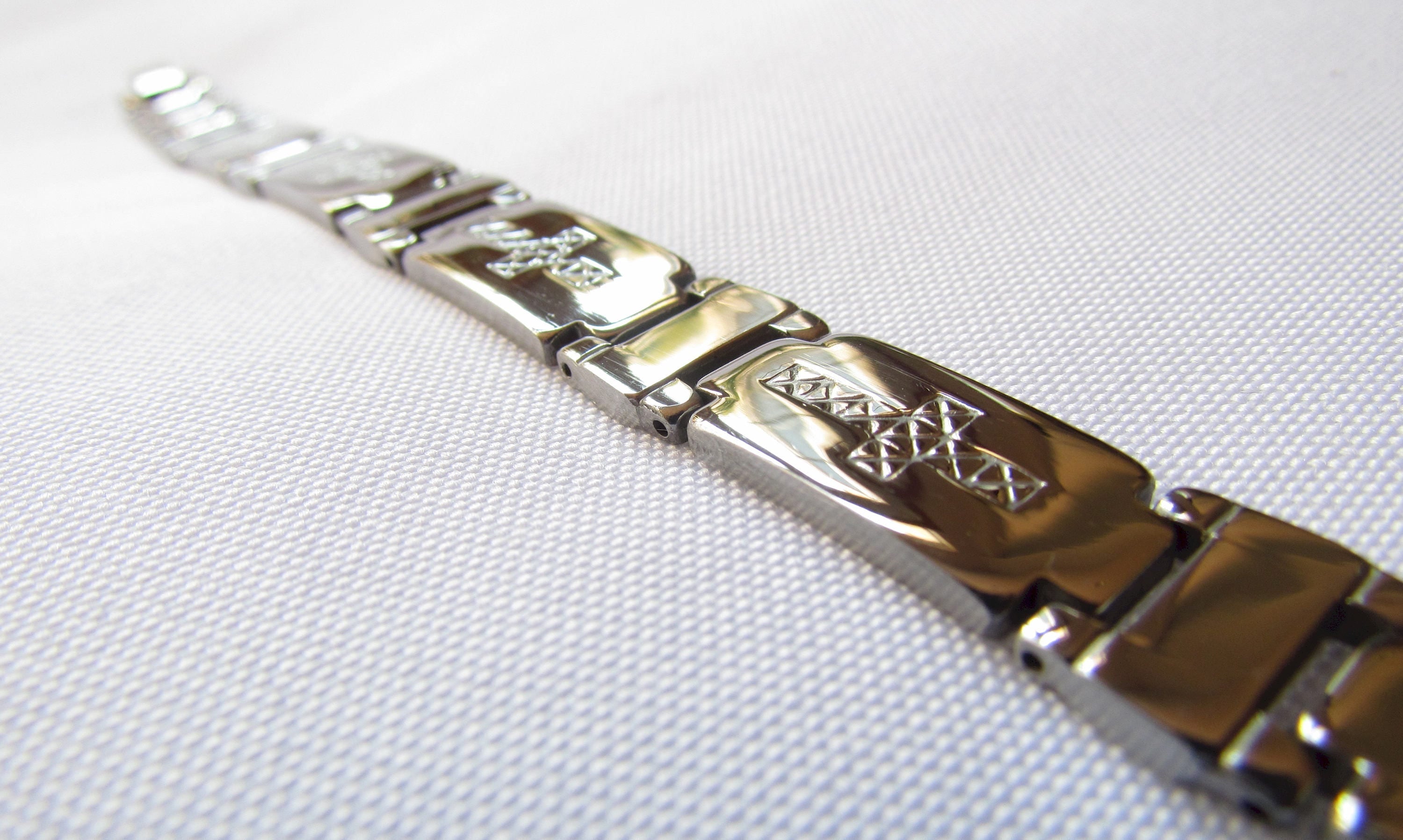 Stainless steel cross bracelet close-up with engraved geometric link segments