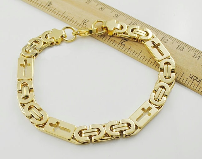 Gold cross charm bracelet with linked chain and round clasp, against ruler