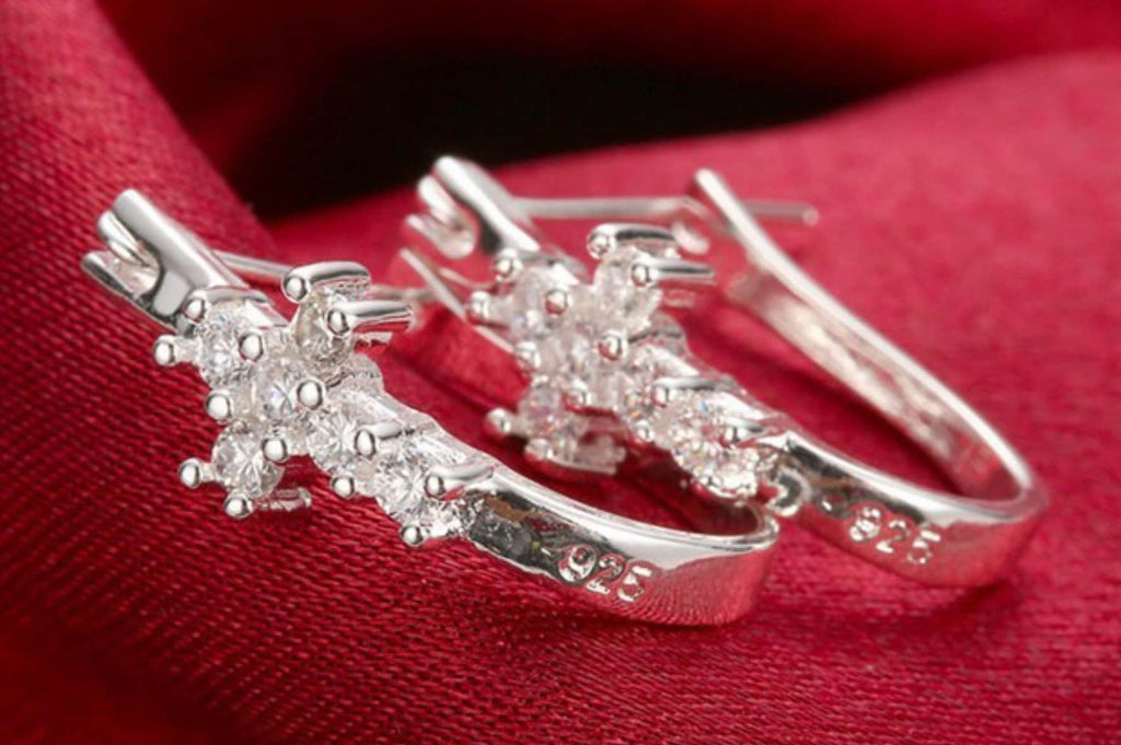 Silver-tone cross huggie earrings with clear CZ clusters on red fabric.