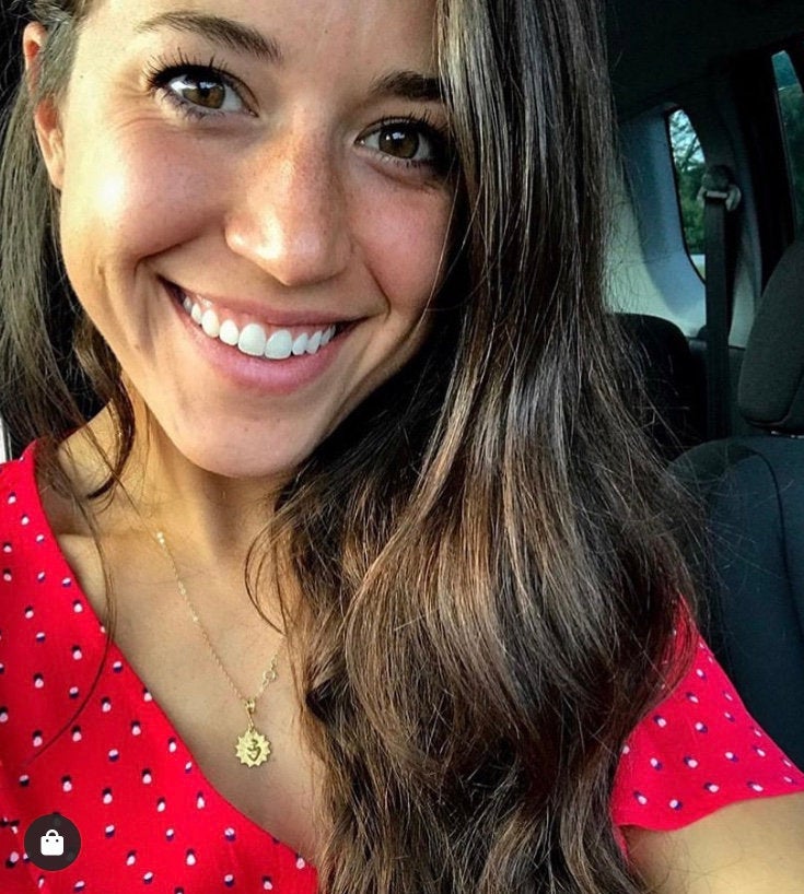 Gold-tone scalloped heart charm necklace worn by a smiling woman in a red dress